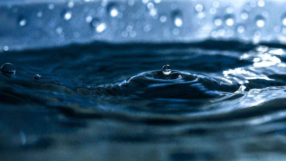 Nahaufnahme von dunkelblauen Wasseroberfläche mit einer einzelnen Welle und einem aufsteigenden Tropfen, umgeben von glitzernden Lichtreflexen im Hintergrund.