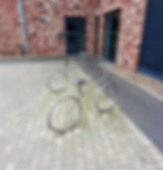 Ein schwarzer Industriecontainer wurde zu einer mobilen Getränkebar umgebaut und steht in einer modernen Werk- oder Industriehalle. Auf der oberen Stirnseite ist gut sichtbar das rote Logo der Marke „Voelkel“ angebracht. Im unteren Bereich ist eine große Öffnung eingelassen, durch die vier rote Kühlschränke mit Voelkel-Branding zu sehen sind. Der Innenraum des Containers ist mit einer gewellten Deckenstruktur und Beleuchtung ausgestattet. Rechts im Bild führen Metalltreppen auf eine Galerieebene, daneben stehen Werkzeuge, Kartons und eine Steuerungseinheit, was auf eine Aufbau- oder Wartungssituation hinweist. Tageslicht fällt durch ein großes, hohes Fenster von rechts ein.