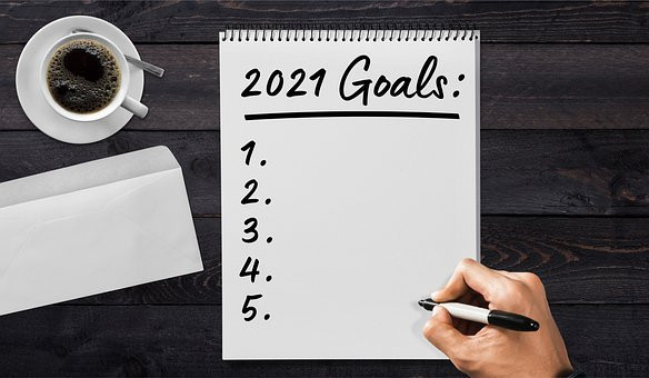 Notepad with 2021 goals being written next to coffee