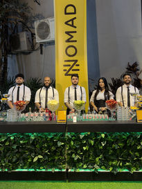 Bar de ativação da marca NOMAD com parede de folhagens verde e bartenders uniformizados