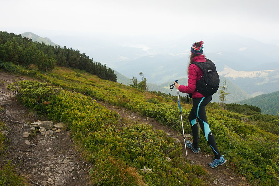 Woman hiking uphill on a mountain trail using trekking poles, wearing a backpack in cold, foggy weather with scenic valley views