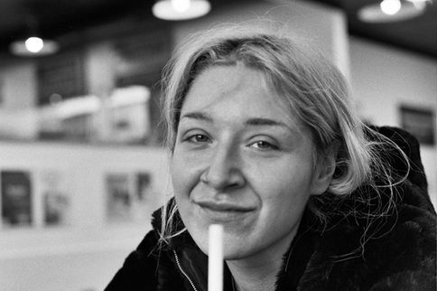A person smiling, holding a straw in black and white. Wojciech J Walkowicz