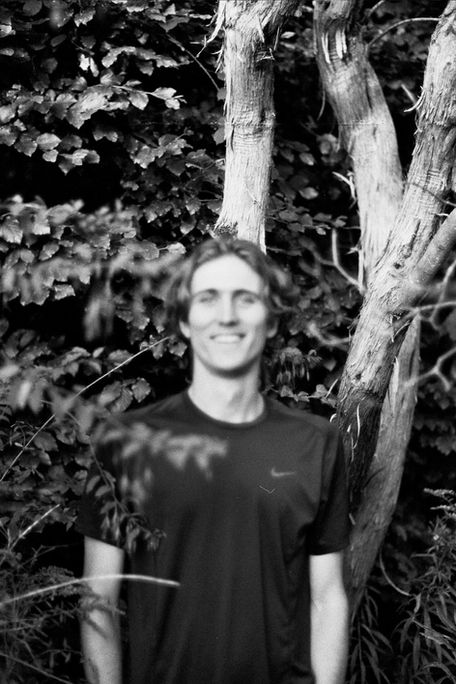 A person standing in a wooded area, smiling. Wojciech J Walkowicz