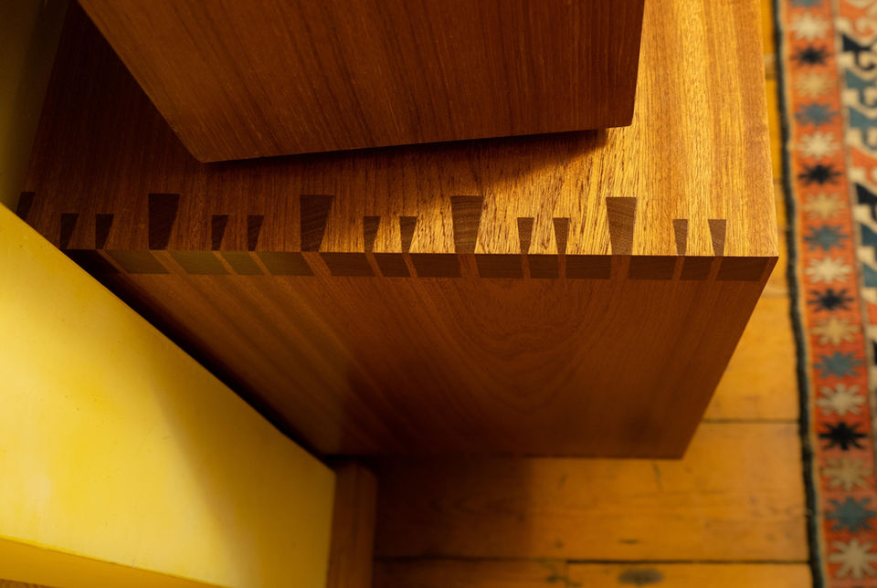 This is a record player stand that is a hifi unit that works as vinyl record storage. It is made from solid wood, with decorative mitred dovetails. It is made from utile which is like mahogany. It's style is mid-century modern. It was a bespoke hifi cabinet to match the Tannoy speakers and turntable.