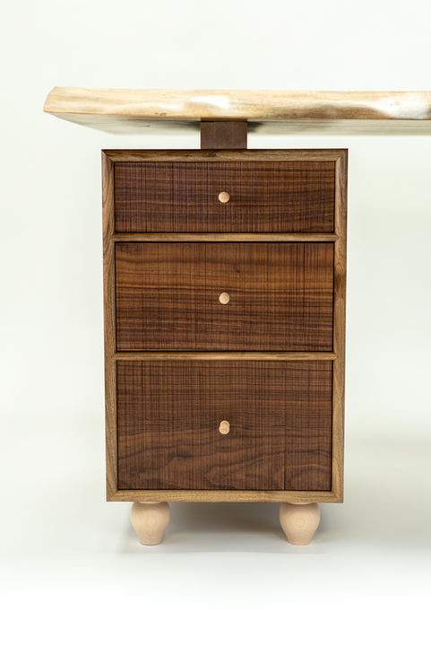 Front view of desk cabinet with textured walnut fronts, and bespoke turned sycamore drawer pulls and legs