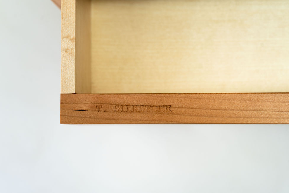 Close-up of maker’s mark stamped into solid cherry on bespoke furniture piece.