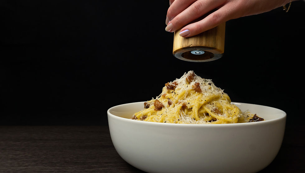 Pastabasta hero carbonara close up white bowl dark surface golden pasta chees guanciale pepper grinder above