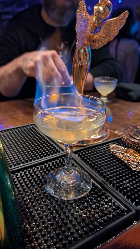 The wych - cocktail absinthe flame in coupe with tower lit fire on bar top