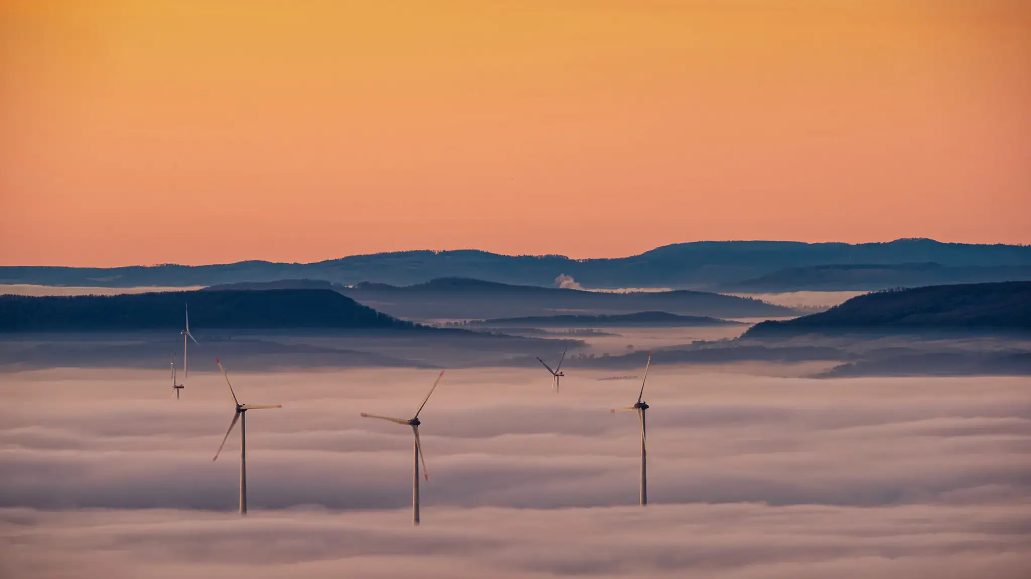 Windräder ragen aus dem Nebelmeer des Harzvorlandes, im Hintergrund Mittelgebirgsketten