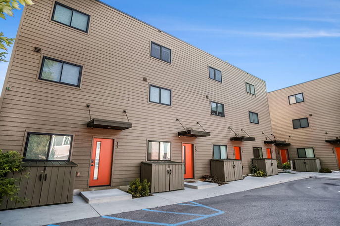 Exterior of townhomes featuring orange doors, brown siding, and multiple windows. 937 Fulton.