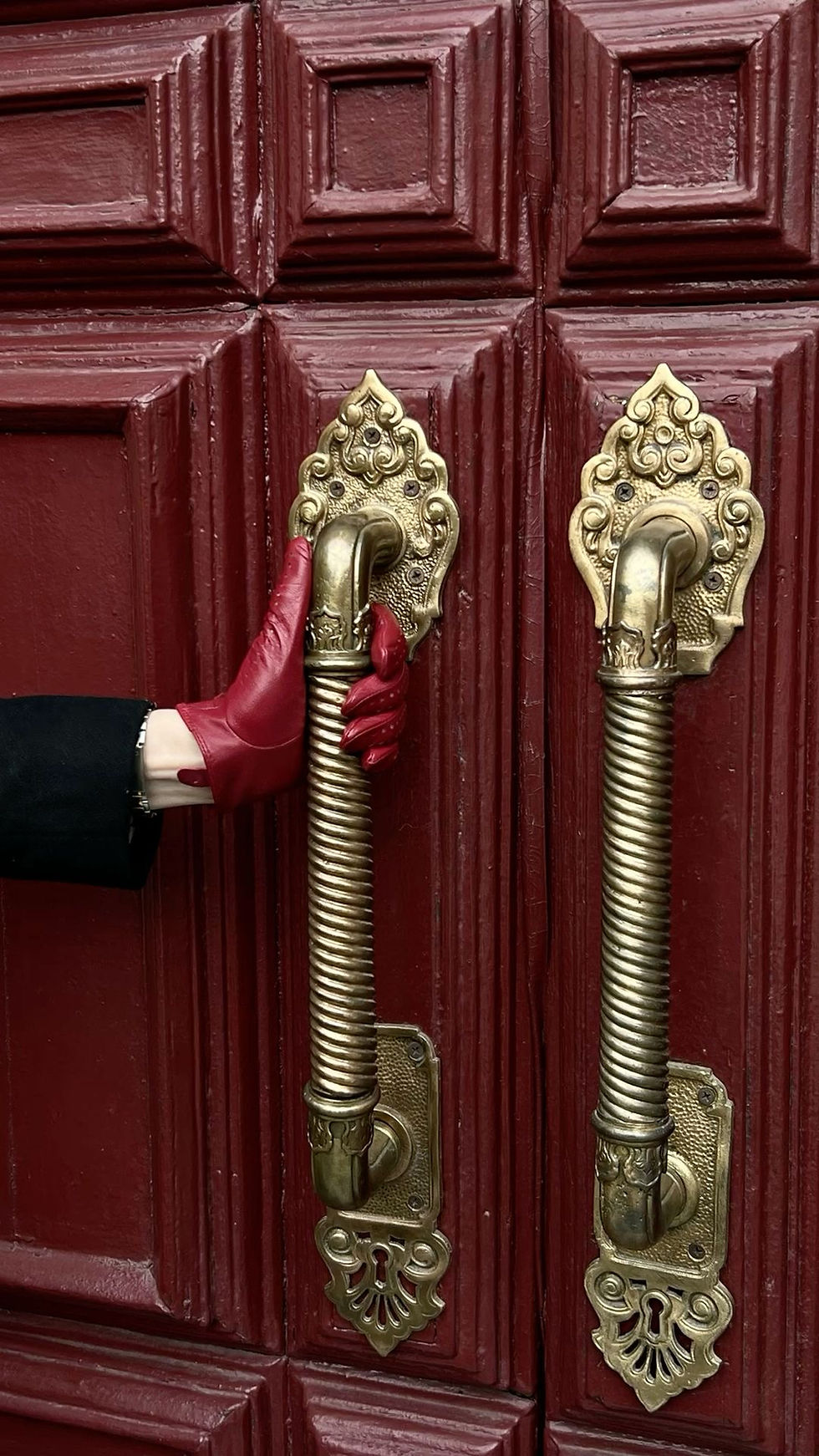 Hand in red glove reaching for golden door handle on red door