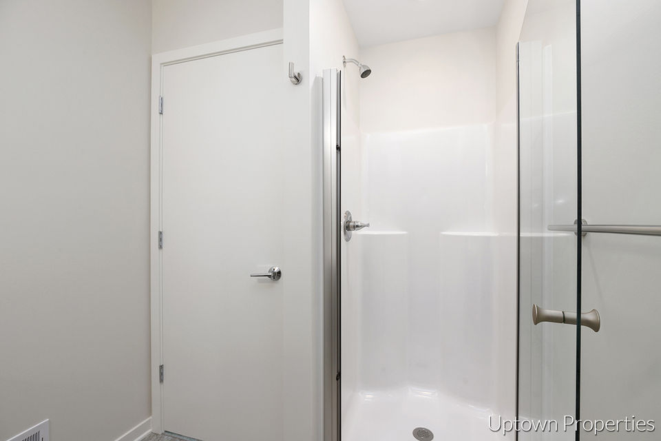 Shower and door inside a modern bathroom with white walls and fixtures.