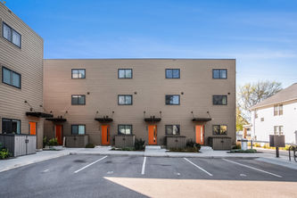 Modern townhomes with bright orange doors and parking under a clear sky.