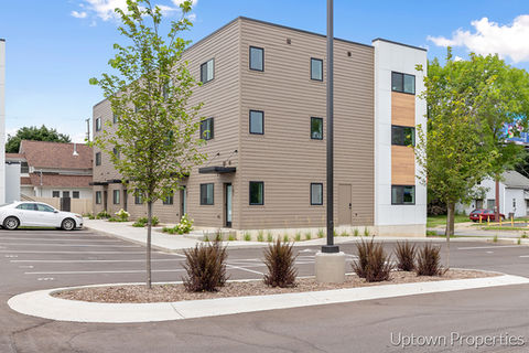 Exterior view of modern apartment building with parking, blue sky background.