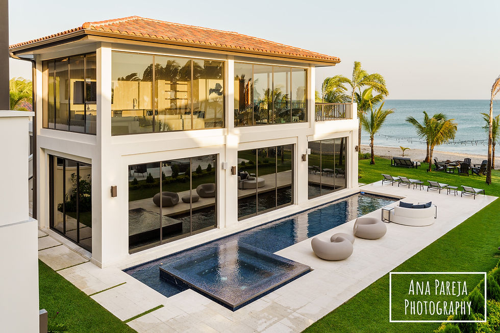 Casa moderna de dos pisos con piscina y terraza frente al mar. Palmera y césped en el fondo. Texto: Ana Pareja Photography.