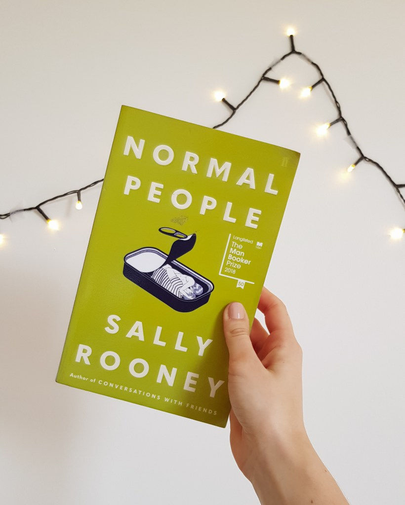 Normal People by Sally Rooney held against white wall with fairy lights