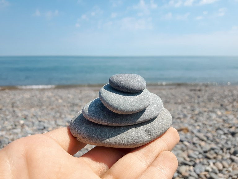 peaceful image of small stones stacked together on hand with the blue sea and sky in the background