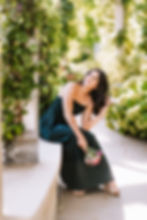 High school senior in a dark green dress holding flowers in a garden walkway