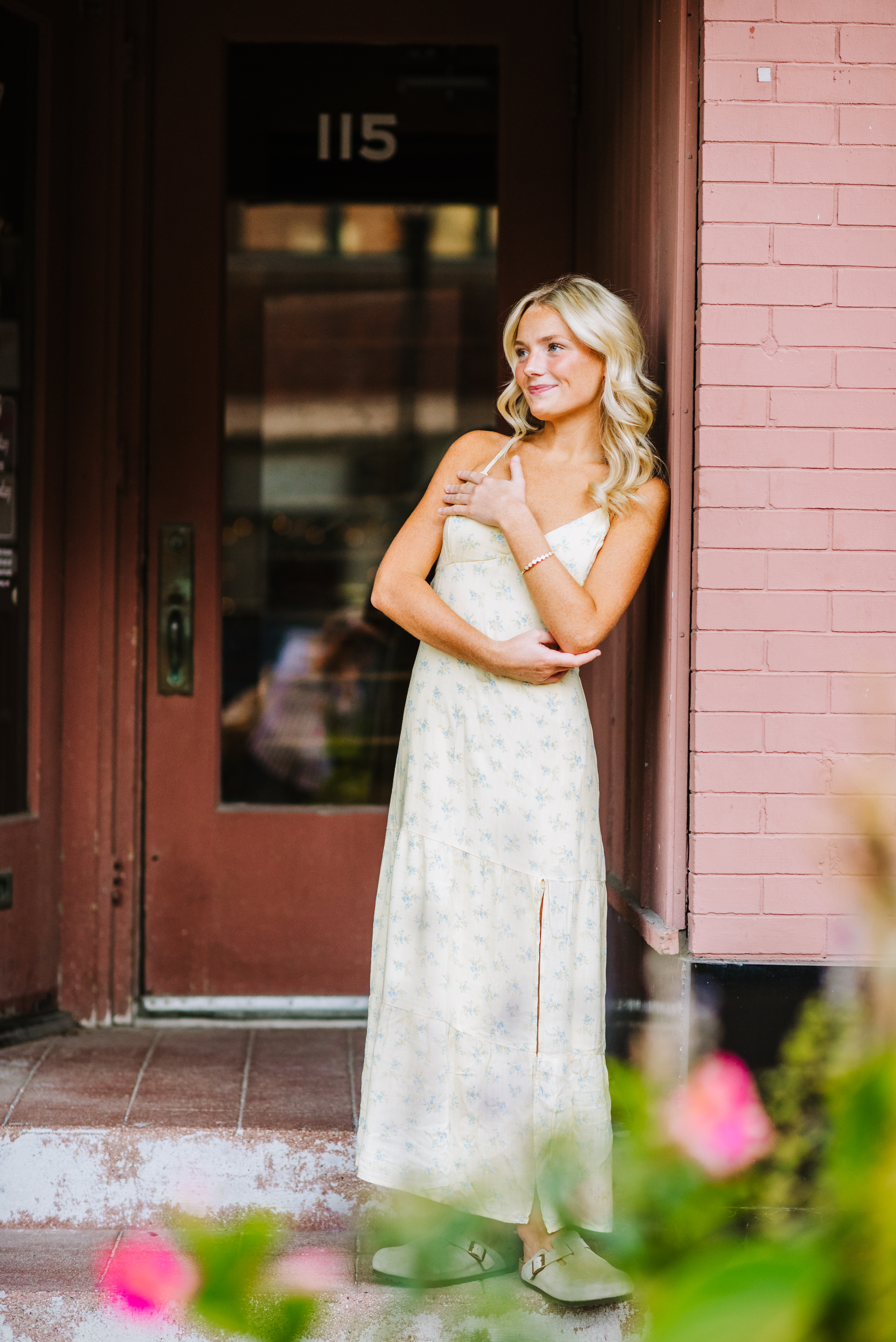 High school senior in a floral maxi dress posing beside a pink brick building