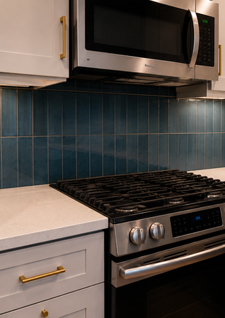 Close-up of blue ceramic tile backsplash behind stainless steel range with white quartz countertops and shaker cabinets.
