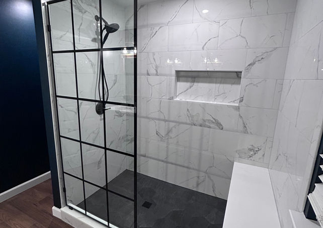 Walk in shower with custom glass panel, white marble tile and shower bench.