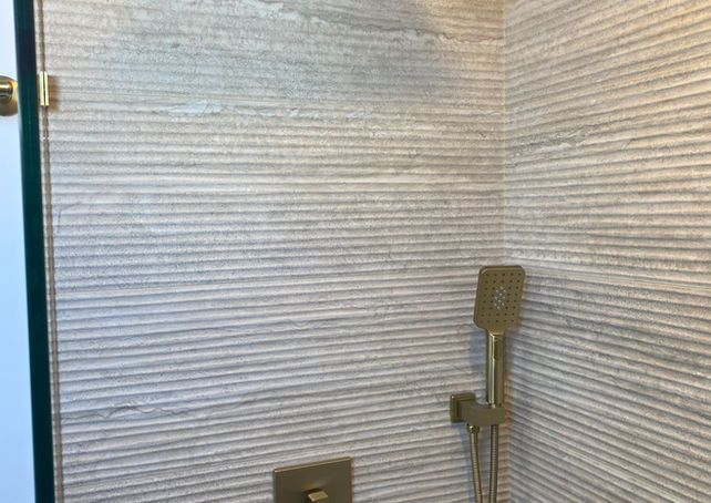 Textured wavy tile with gold tile trim and gold shower fixture