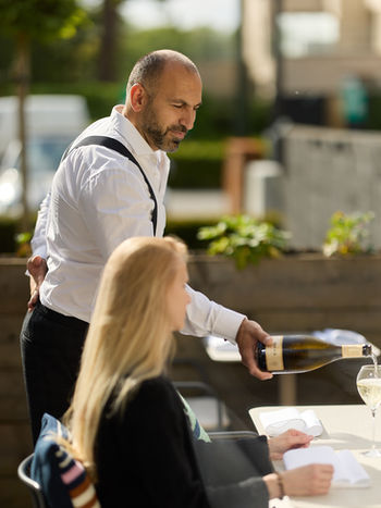 Garik serveert één van de geselecteerde wijnen op het zonnig terras van Alcomo in Schilde