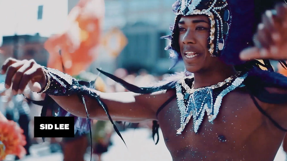 Danseur en costume orné de perles, bras levés lors d’un défilé en plein air; fond flou, texte SID LEE.