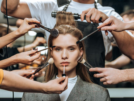 Model with multiple hair and makeup artists applying makeup to her face and styling her hair at the same time
