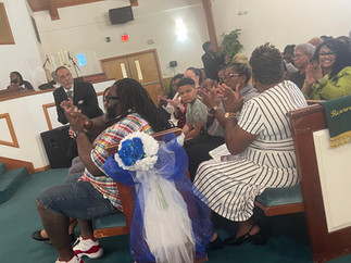 Pastor Thompson's family seated in front rows, blue and white ribbon hanging on pew