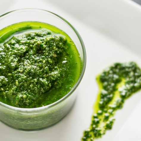 Glass jar of green carrot top pesto on a white plate with a pesto smear beside it. Bright, fresh, and appetizing look.