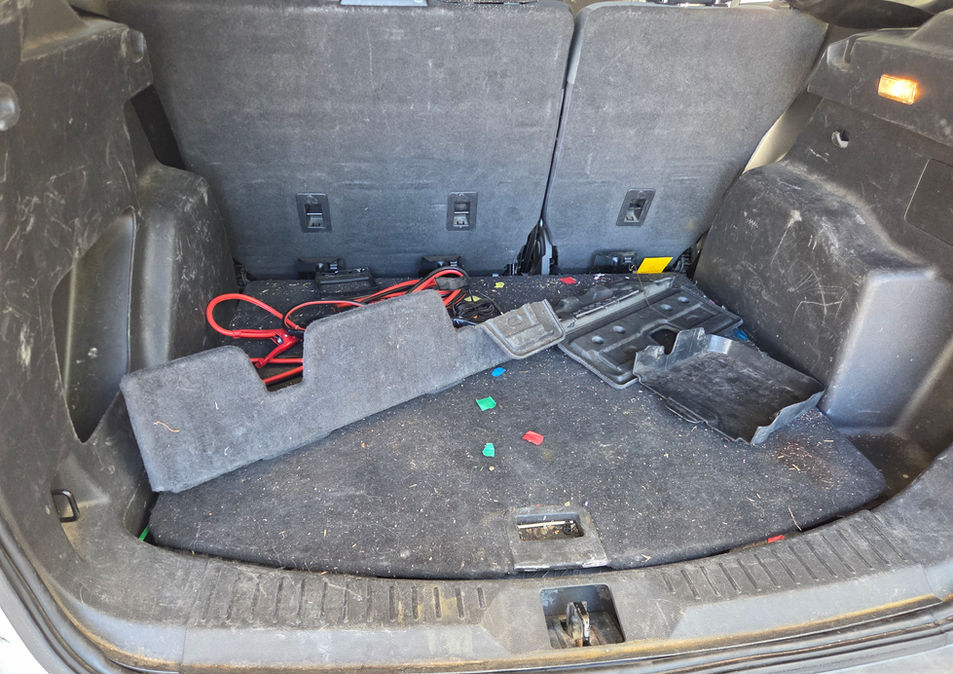 Messy car trunk with red cables and loose floor mat.