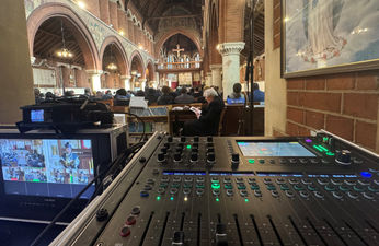 An audio mixer in the foreground with a funeral service in the background