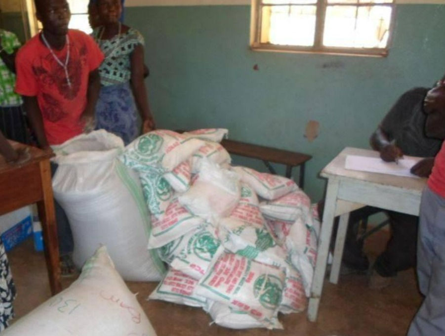 Jerry (left in red) standing with mounds of food bags such as rice and flour.