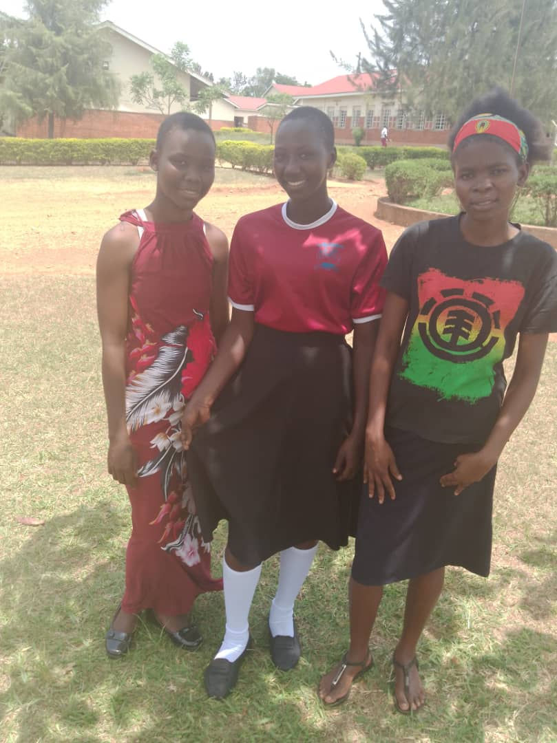 Three black women stand in front of a university in Uganda.