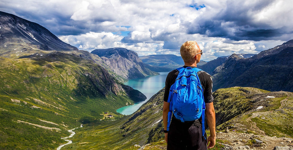 Blond hiker wearing a blue backpack and sunglasses looks over a valley in Scandinavia