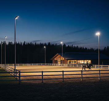 Reitplatz im Dunkeln mit Reiter und Stall im Hintergrund