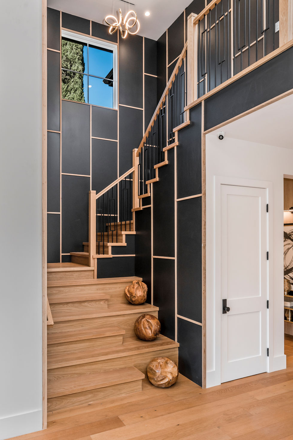 Modern luxury staircase in Los Angeles featuring natural wood steps, black metal railing, geometric wall paneling, and contemporary architectural design.