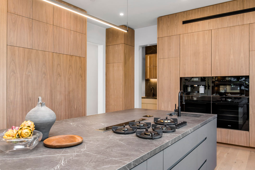Modern luxury kitchen in Los Angeles new construction home featuring oversized waterfall island, custom wood cabinetry, recessed lighting, and large sliding glass doors to backyard.