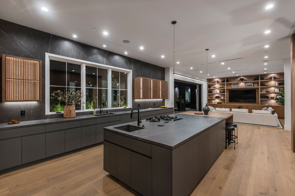 Modern luxury kitchen in Los Angeles new construction home featuring oversized waterfall island, custom wood cabinetry, recessed lighting, and large sliding glass doors to backyard.