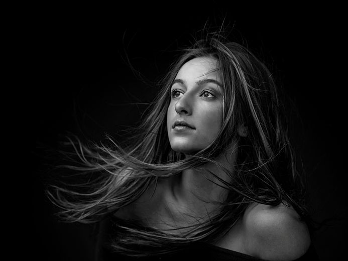 Portrait artistique en noir et blanc d’une femme aux cheveux au vent, réalisé en studio à Longueuil.