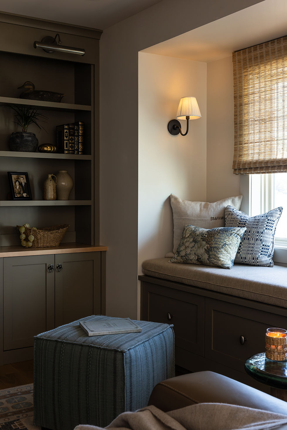 Built-in window seat with blue cushions, dark shelving, and a woven shade