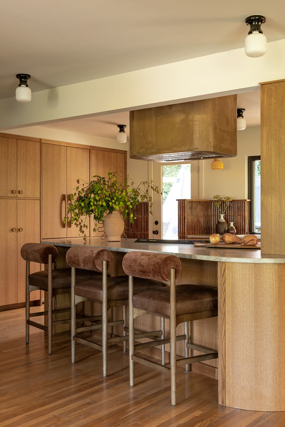 Curved kitchen peninsula with upholstered barstools and warm oak cabinetry