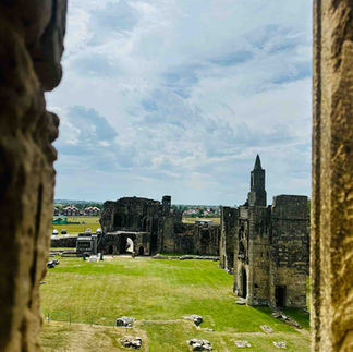 A view through a stone window of a medieval stone tower in a field of freshly mowed grass