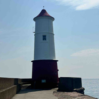 A white lighthouse with red trim down a paved pier next to the river