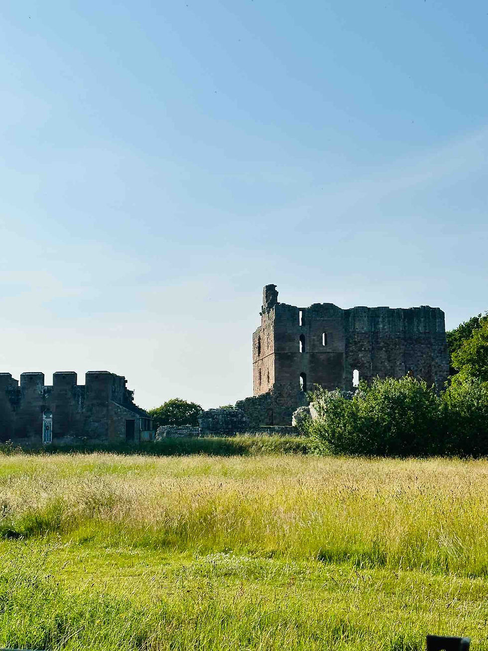Stone castle ruins, roofless, in a field of green grass under a clear blue sky