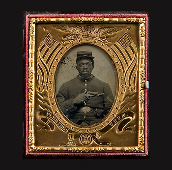 In black thermoplastic case with brass hinges and red velvet liner; Preserver and mat: brass decorated with eagle, 2 American flags, cannon, and E Pluribus Unum set in a red velvet liner; tintype with cover glass of an African American Union soldier with a moustache and beard, holding a pistol across his chest. His buttons and belt buckle are hand-colored in gold paint. The hand-coloring on the buckle reads backwards "SU," which when considered that the image is reversed, reads "US," the traditional inscription on Union Civil War belt buckles.