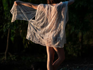Woman waving white cloth in mystical nature at dusk, embodying freedom and sensuality.