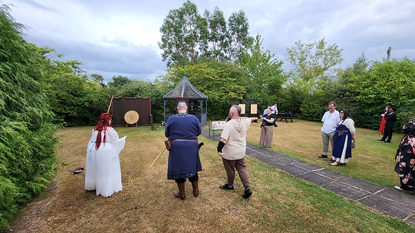 a bride and groom stood at the axe range ready to throw an axe. The bride is wearing all white, groom is wearing civilian vik