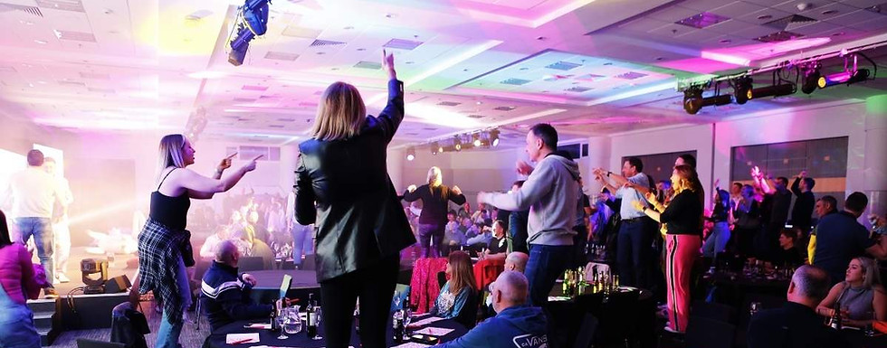 People dancing, singing and standing on chairs at Introducing Events party bingo corporate entertainment experience. The conference room is filled with coloured disco lights in a full-on party atmosphere.